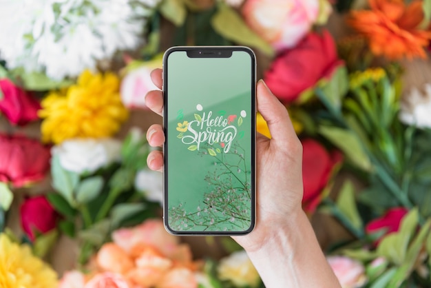 PSD hand holding smartphone mockup above flowers