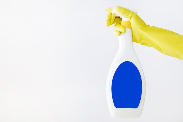 Hand in yellow glove holds spray bottle of liquid detergent. 