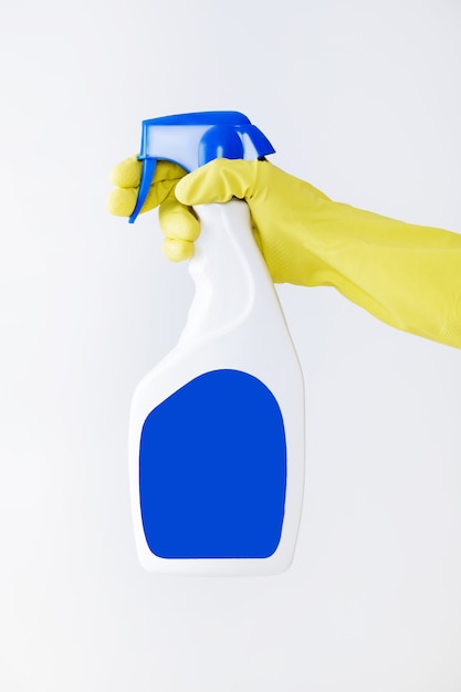 Hand in yellow glove holds spray bottle of liquid detergent. 