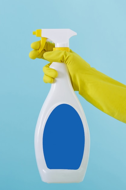 La mano in un guanto giallo tiene una bottiglia spray di detergente liquido.