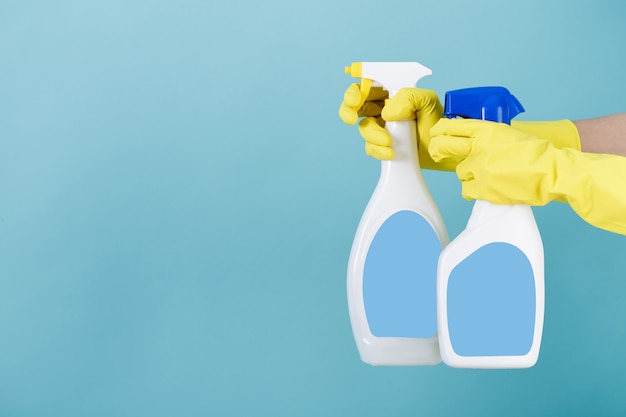 Hand in yellow glove holds spray bottle of liquid detergent. 