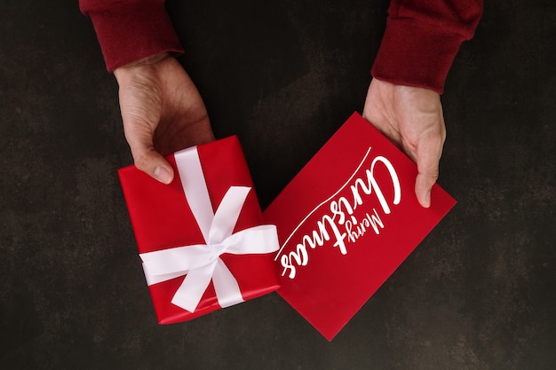 PSD hands holding merry christmas greeting card mockup template and gift box.