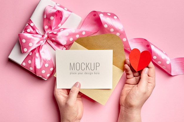 Hands holding valentine's day card mockup with gift box and paper heart