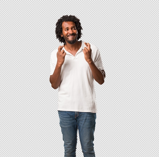 handsome african american crossing his fingers, wishes to be lucky for future projects, excited but worried, nervous expression closing eyes