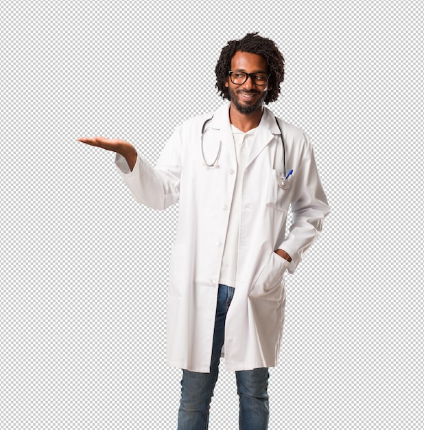 Handsome african american medical doctor holding something with hands, showing a product, smiling and cheerful, offering an imaginary object