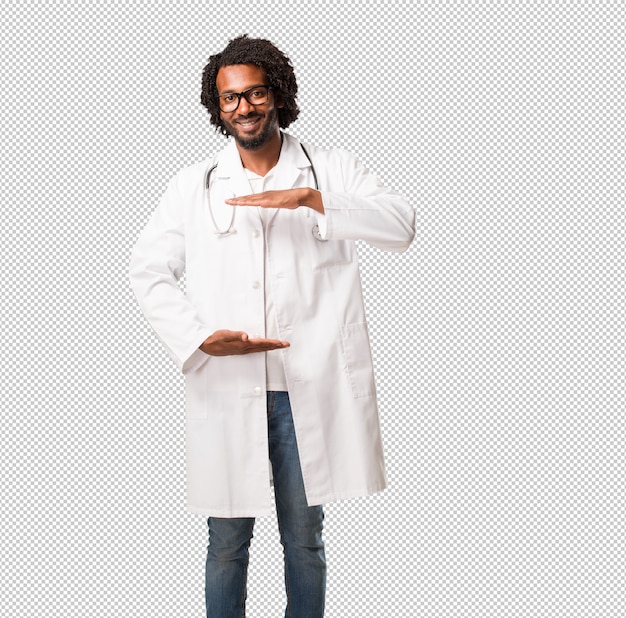 Handsome man medical doctor holding something with hands, showing a product, smiling and cheerful, offering an imaginary object