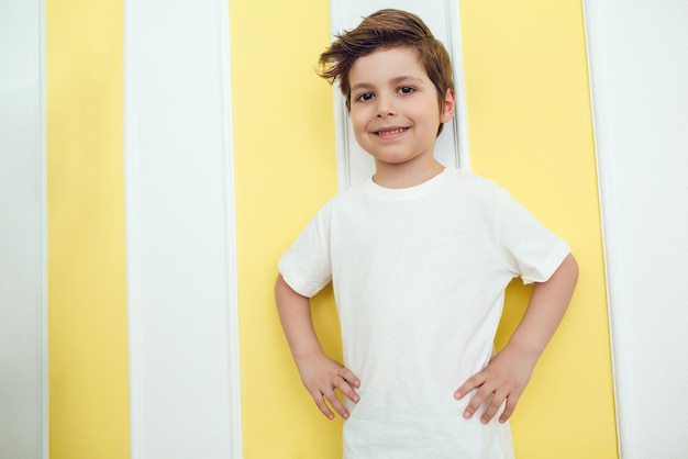 Happy boy posing with hands on hips in front of yellow and white striped wall