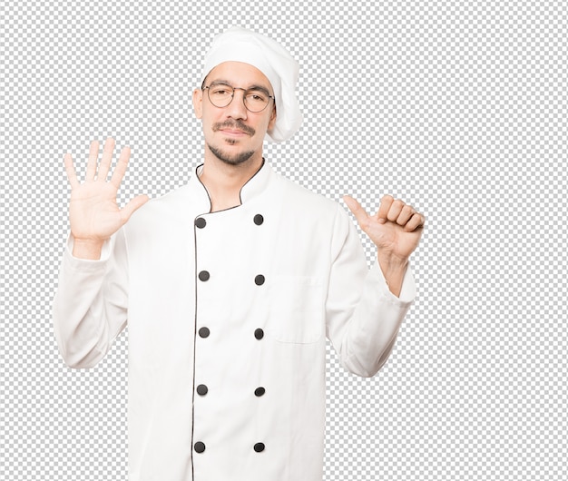 Happy young chef doing a number six gesture with his hands