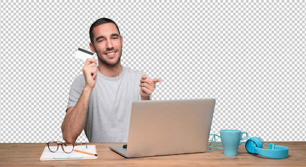 PSD happy young man sitting at his desk and holding a credit card