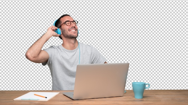 Happy young man sitting at his desk and using a headphones