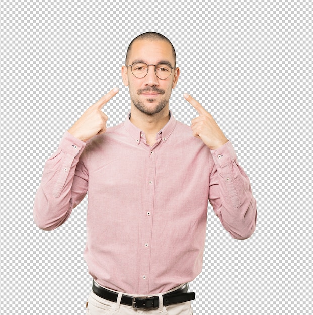 Hesitant young man making a gesture of being careful with his hand pointing at his eye