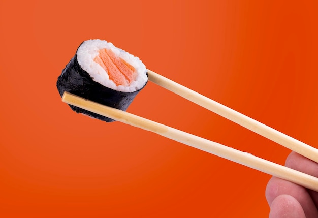 オレンジ色の背景にチョップスティックを貼ったウルーマキ寿司ロールを握る