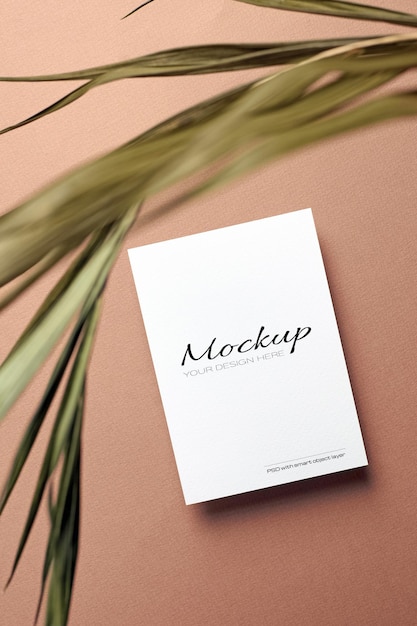 Invitation card or flyer, stationary mockup with dry nature palm leaf on beige paper background