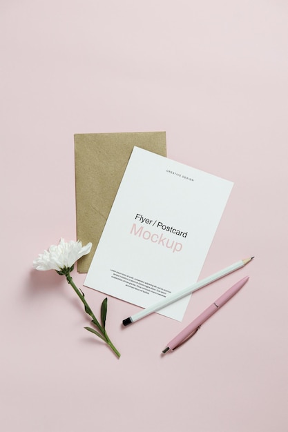 Mockup di biglietto d'invito con fiore bianco e cancelleria su sfondo rosa