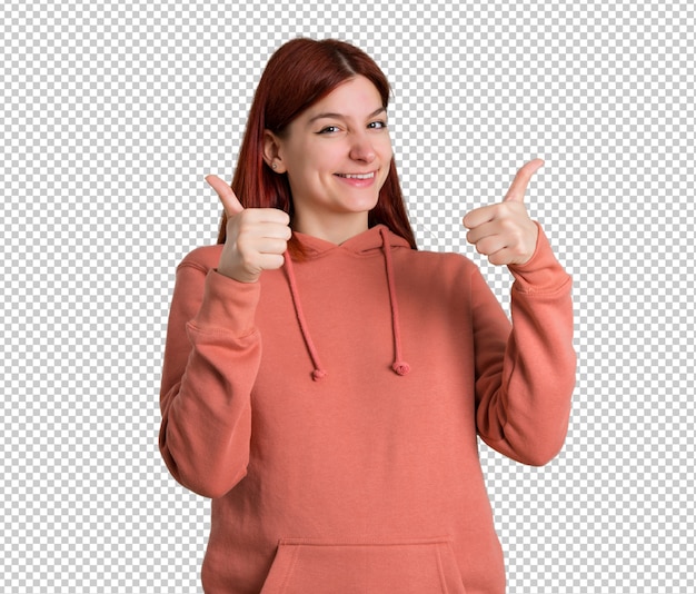 Jong roodharigemeisje met roze sweatshirt die duimen op gebaar met beide handen geven