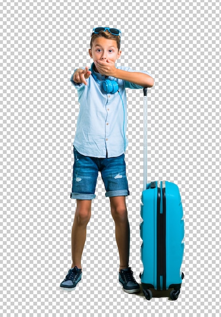 Kid with sunglasses and headphones traveling with his suitcase pointing