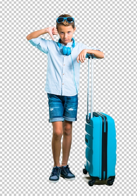 Kid with sunglasses and headphones traveling with his suitcase showing thumb down sign