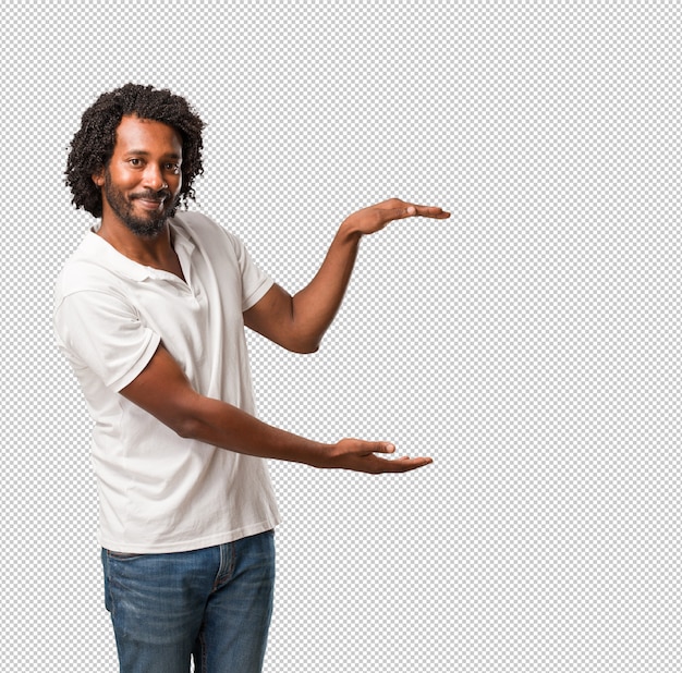 Knappe Afrikaanse Amerikaan die iets met handen houden, een product tonen, glimlachend en vrolijk, die een denkbeeldig voorwerp aanbieden