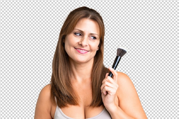 PSD kobieta w średnim wieku na odosobnionym tle trzymająca szczotkę do makijażu i patrząca w górę