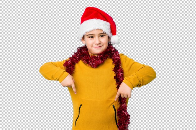 サンタ帽子をかぶっているクリスマスの日を祝う小さな男の子は、指で肯定的な感じでポイントを分離しました。