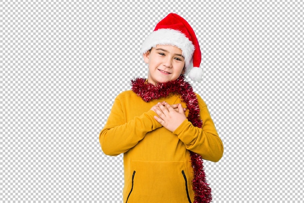 Little boy celebrating christmas day wearing a santa hat isolated has friendly expression, pressing palm to chest. Love concept.