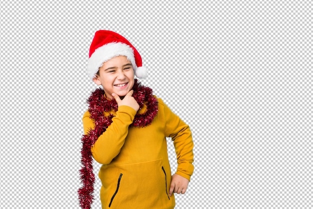 PSD little boy celebrating christmas day wearing a santa hat isolated looking sideways with doubtful and skeptical expression.