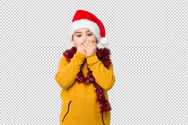 Little boy celebrating christmas day wearing a santa hat isolated shocked covering mouth with hands.