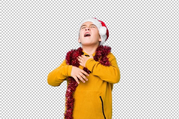 Little boy celebrating christmas day wearing a santa hat laughs happily and has fun keeping hands on stomach.