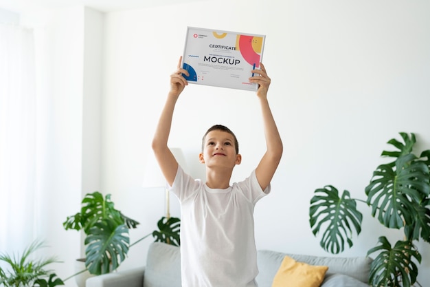 PSD little boy at home holding a certificate mock-up