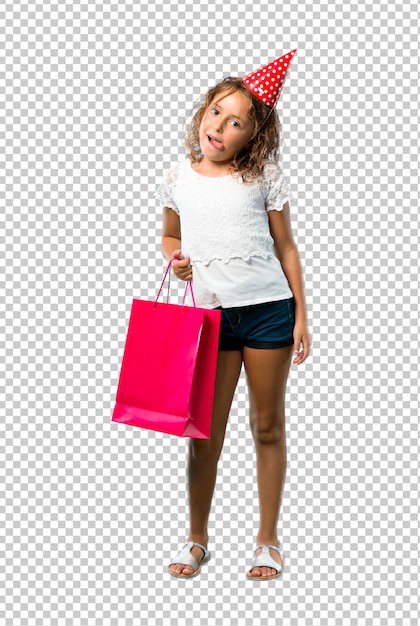 Little girl at a birthday party holding a gift bag showing tongue at the camera having funny look