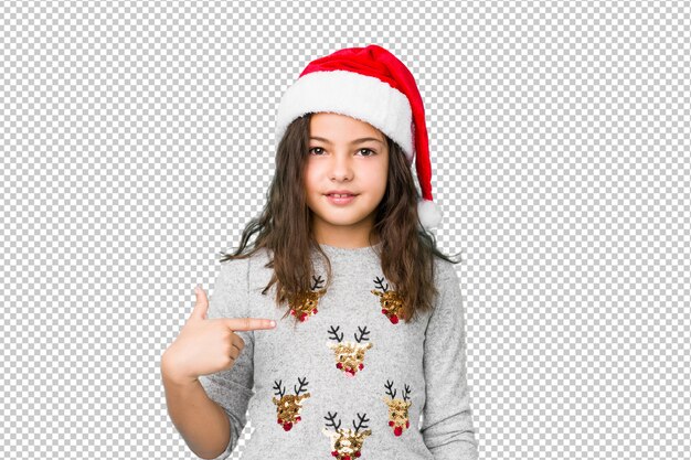 Little girl celebrating christmas day person pointing by hand to a shirt copy space, proud and confident