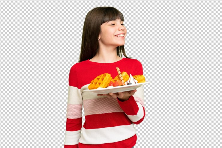 PSD little girl holding waffles over isolated chroma key background laughing in lateral position