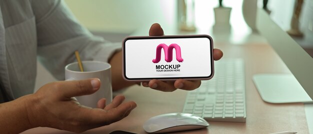 Imprenditore maschio che mostra smartphone schermo orizzontale mockup sulla scrivania in ufficio