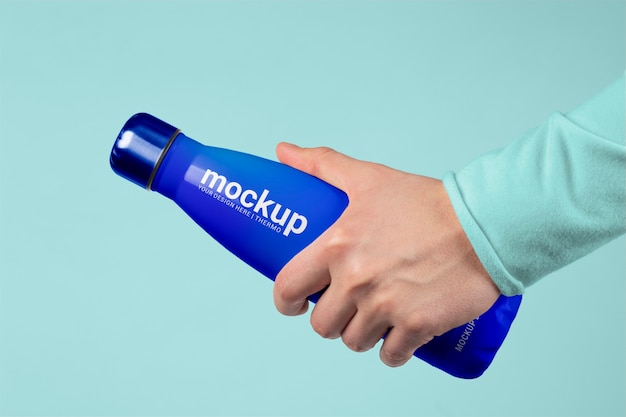 Mano maschio che tiene mock-up di bottiglia thermos blu