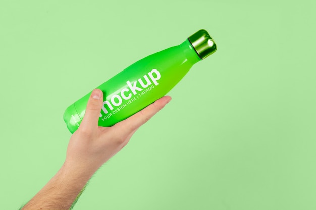 PSD male hand holding mock-up of green thermos bottle