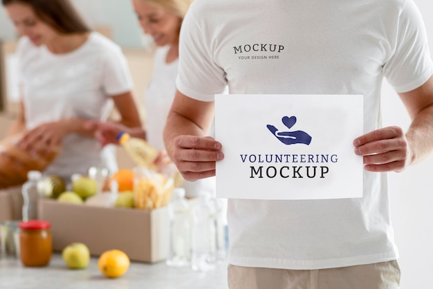male volunteer holding blank paper with women preparing boxes of food donations