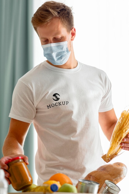 Male volunteer with medical mask preparing food donation box