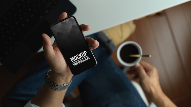 Uomo che tiene smartphone mockup mentre beve il caffè nell'area di lavoro