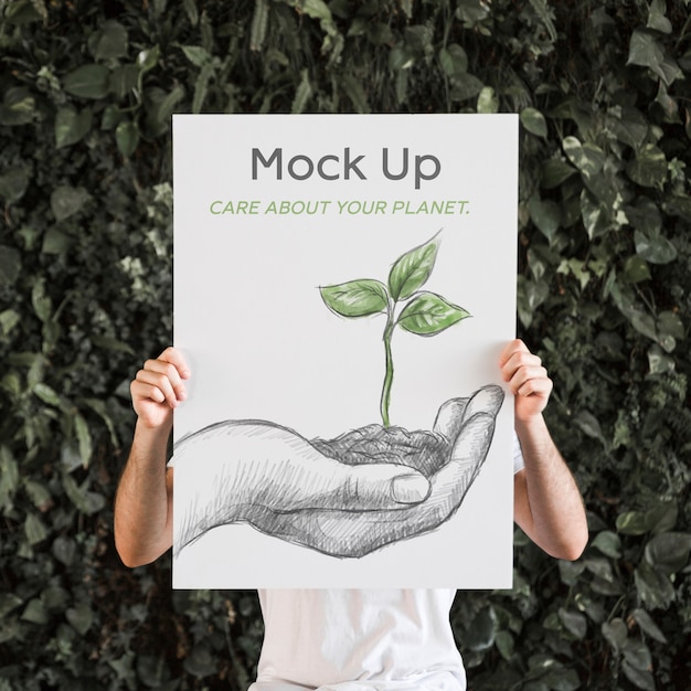 Man presenting poster mockup in front of leaves