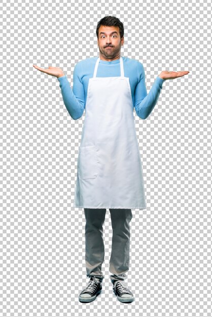 Man wearing an apron having doubts and with confuse face expression while raising hands