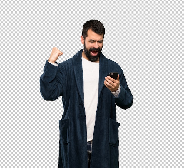 Man with beard in pajamas with phone in victory position