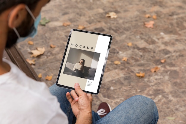 Man with mask on street reading book on tablet