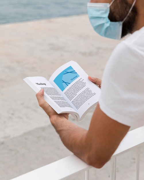 Man with mask on street reading book