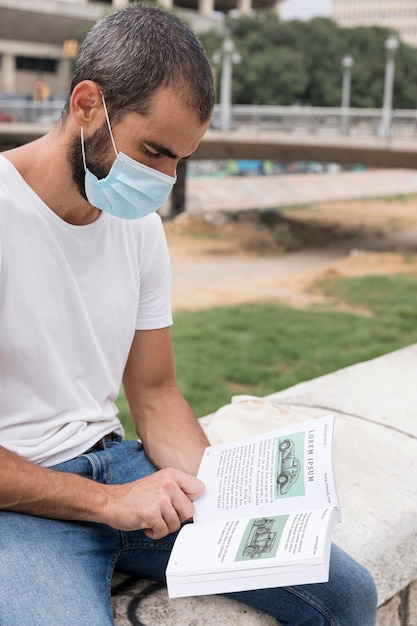 PSD man with mask on street reading book