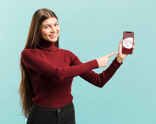 Ragazza felice del colpo medio che indica al suo telefono