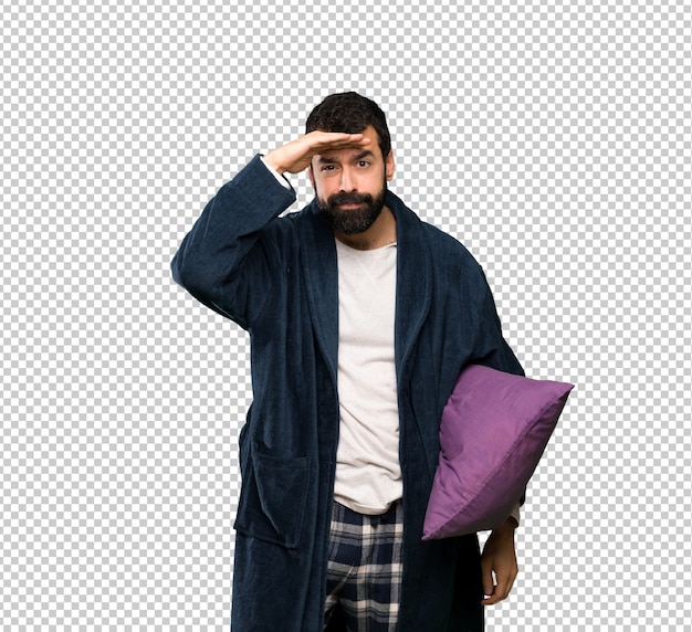 Mens die met baard in pyjama's ver weg met hand kijken om iets te kijken