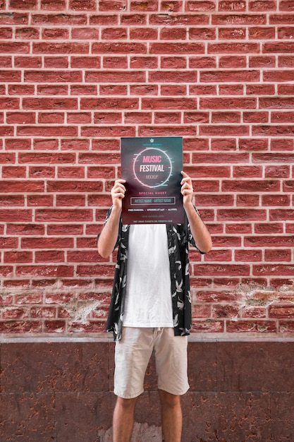 Mężczyzna przedstawia plakatowego mockup przed ściana z cegieł