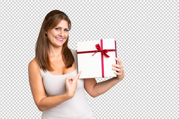 PSD middle age caucasian woman holding a gift over isolated background and pointing it