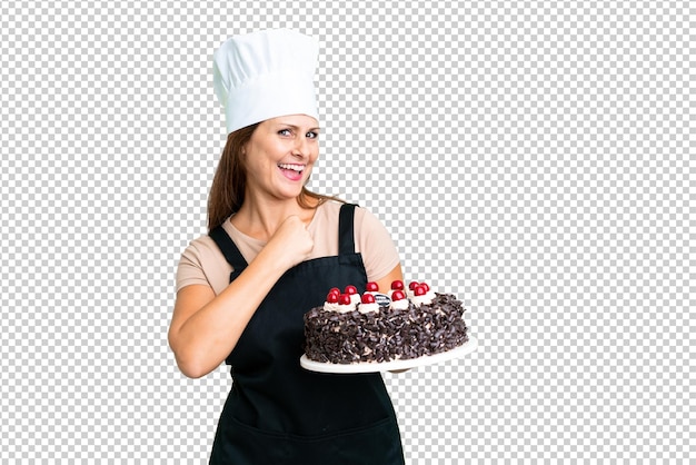 Middle age pastry chef woman holding a big cake over isolated background celebrating a victory