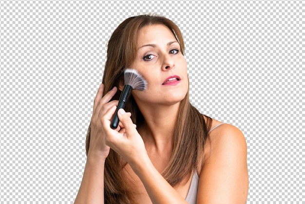 Middle age woman over isolated background holding makeup brush
